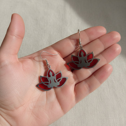 A pair of silver-toned dangle earrings featuring lotus-shaped cutouts filled with red and pink marbled resin, suspended from silver fishhook wires on a light gray background.
