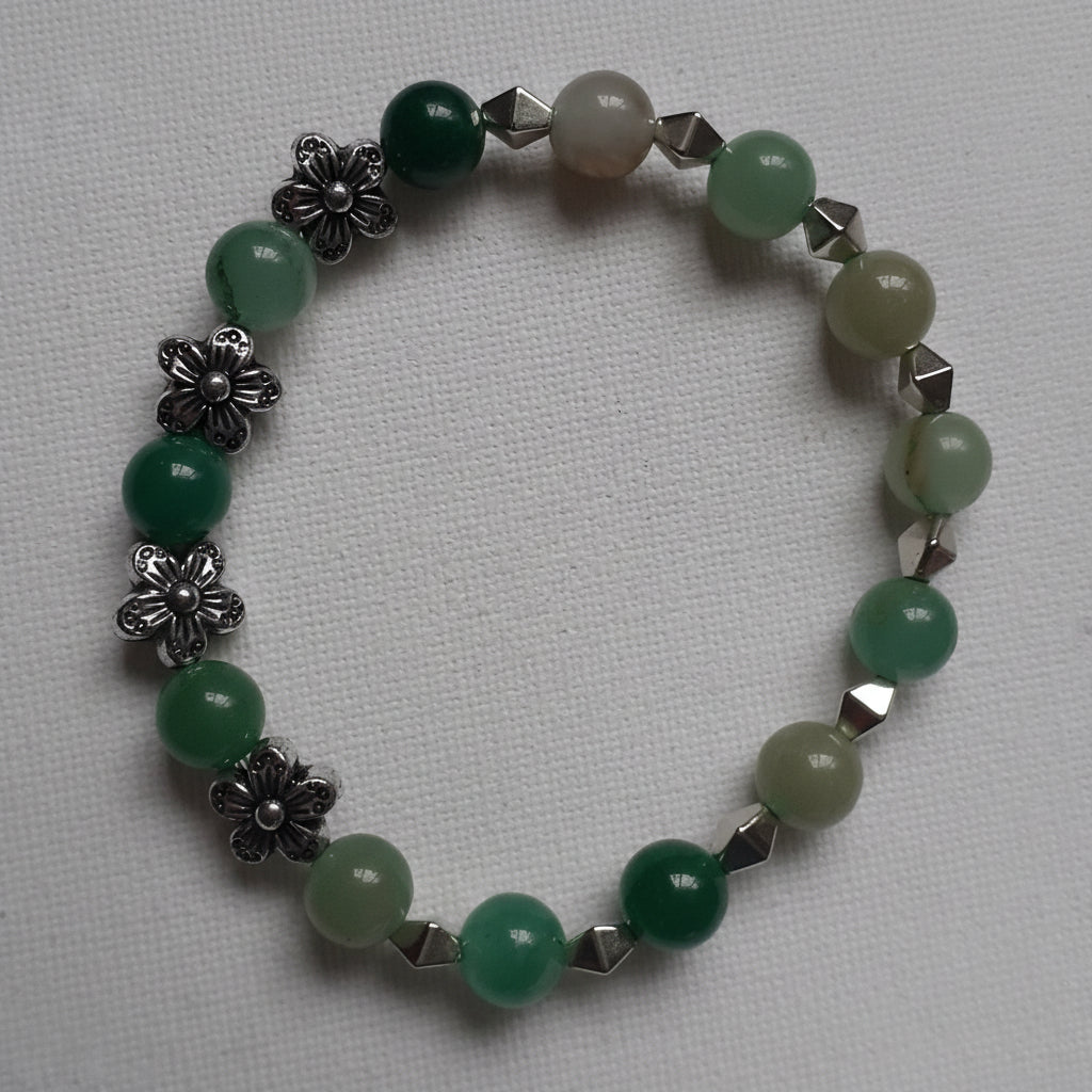 Green beaded bracelet with silver floral and geometric accents on a light gray background