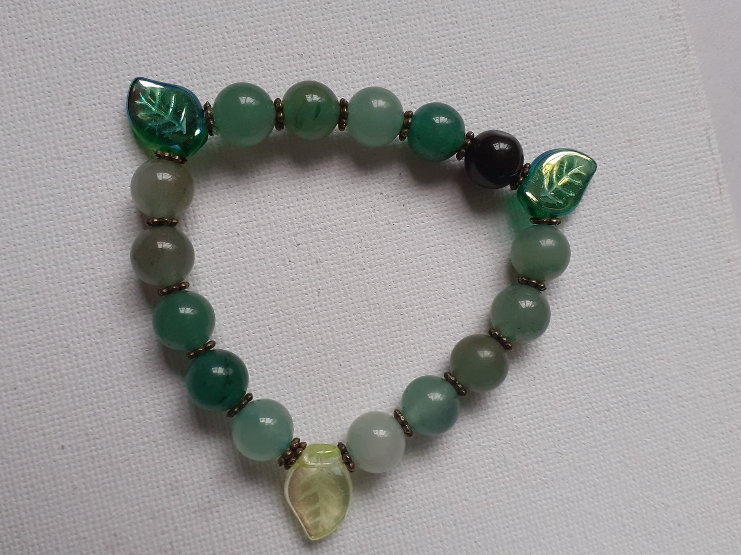 Green beaded bracelet with leaf-shaped beads on a light gray background