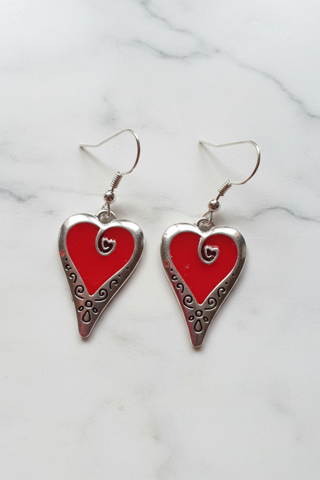 Heart-shaped earrings with red centers and silver borders on a pink background