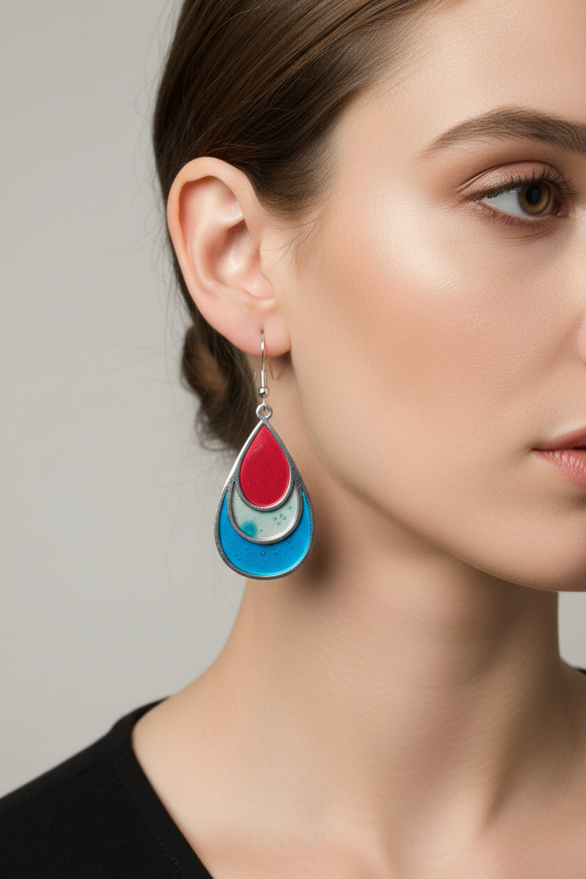 Teardrop-shaped earrings with red, blue, and gold layers on a pink
