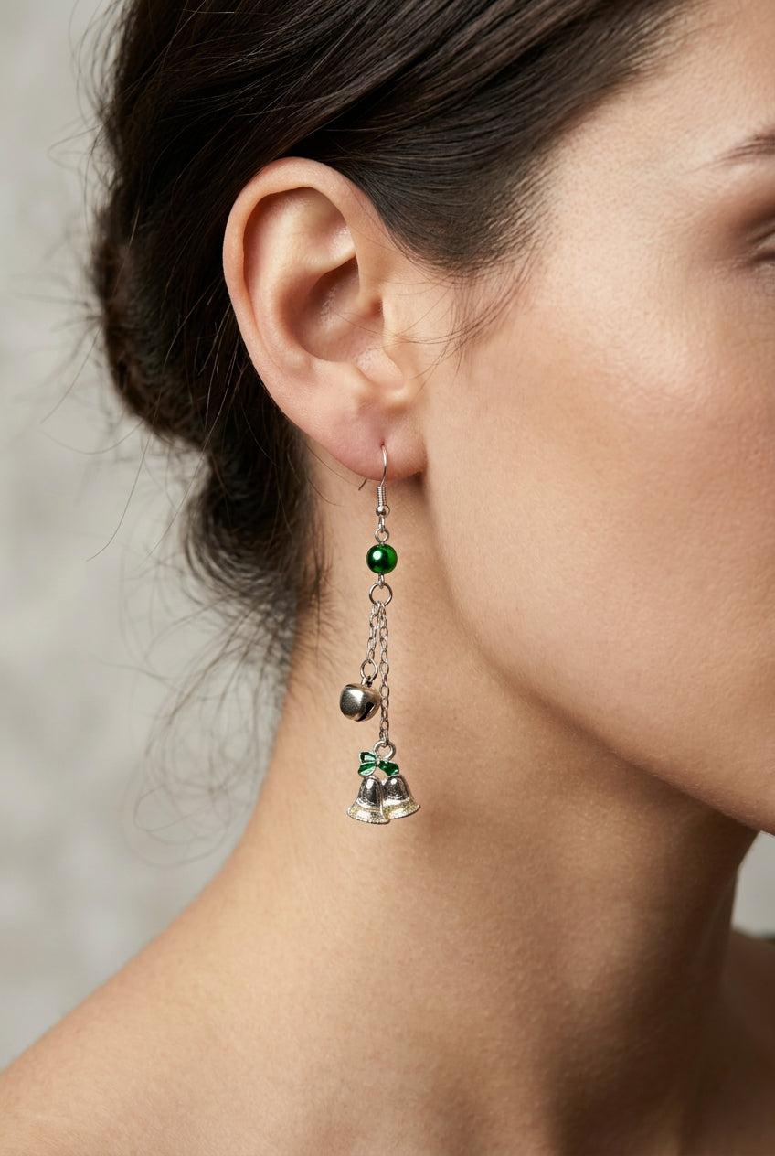 A pair of dangling earrings with silver-tone fishhook wires, green faceted beads, small silver bells, and gold-tone bell charms with green clover details, shown on a plain light background.