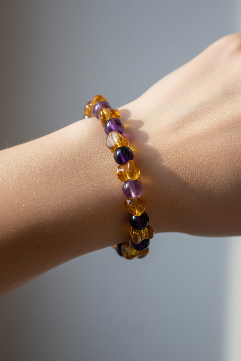 A beaded stretch bracelet featuring alternating translucent amber-yellow and deep purple beads, displayed on a plain light gray surface.