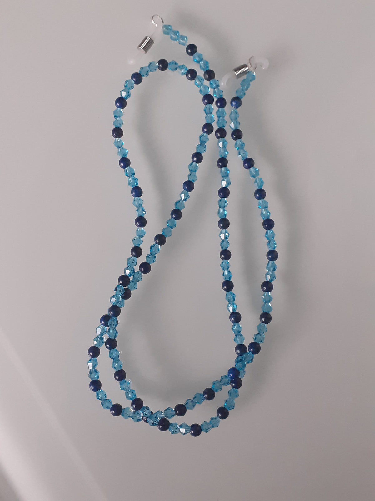 A beaded necklace made of alternating light blue and dark navy blue faceted beads, with silver-toned metal clasps on a plain light gray background.