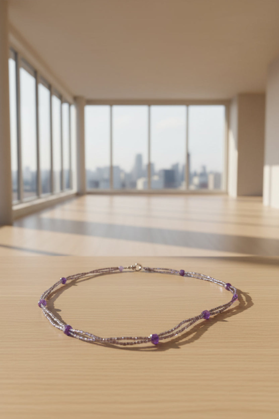 Beaded necklace on a wooden surface with a cityscape view through large windows.