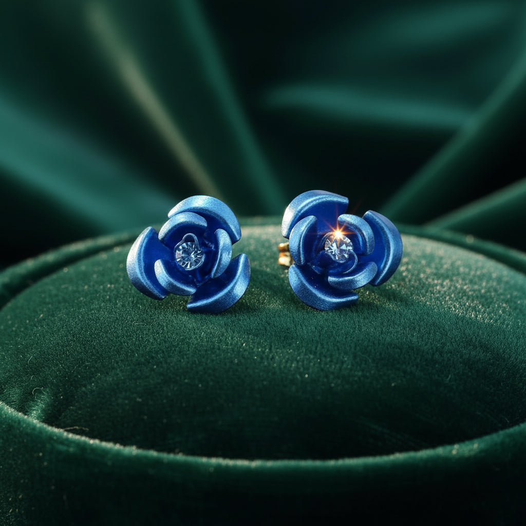 A pair of small blue flower-shaped stud earrings displayed on a black felt jewelry box insert, photographed against a warm beige background.