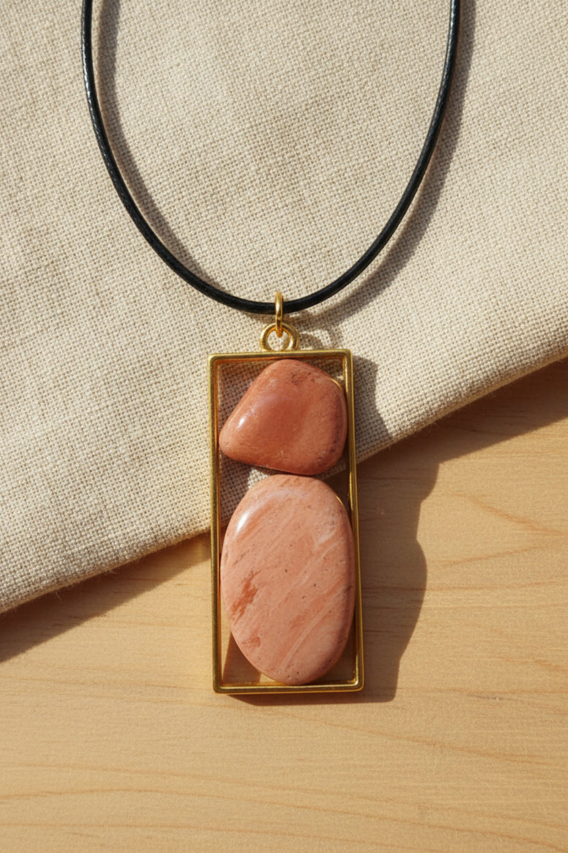 Necklace with two pink stones in a gold frame on a light purple background
