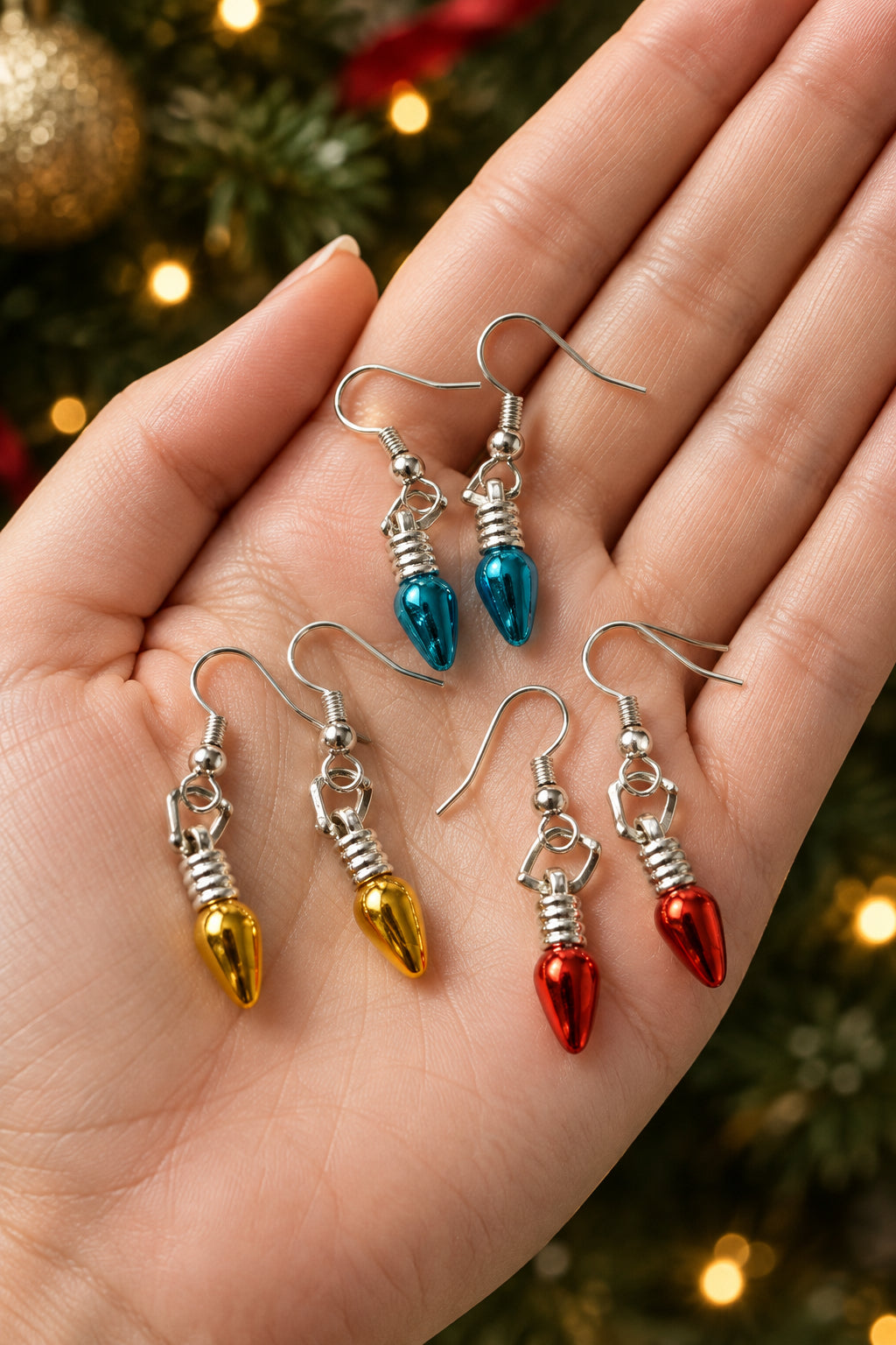 Three pairs of dangling earrings on a plain light background. Each pair has silver-tone fishhook ear wires with a small silver spacer and a teardrop-shaped bead in a different color: blue, gold, and red.