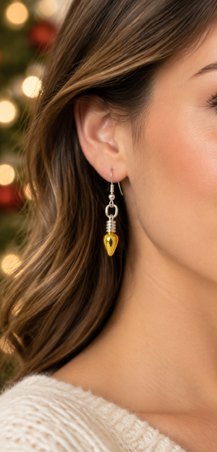 A pair of handmade dangle earrings featuring metallic gold teardrop-shaped beads wrapped in silver wire, suspended from silver fishhook ear wires, displayed on a light gray textured background.