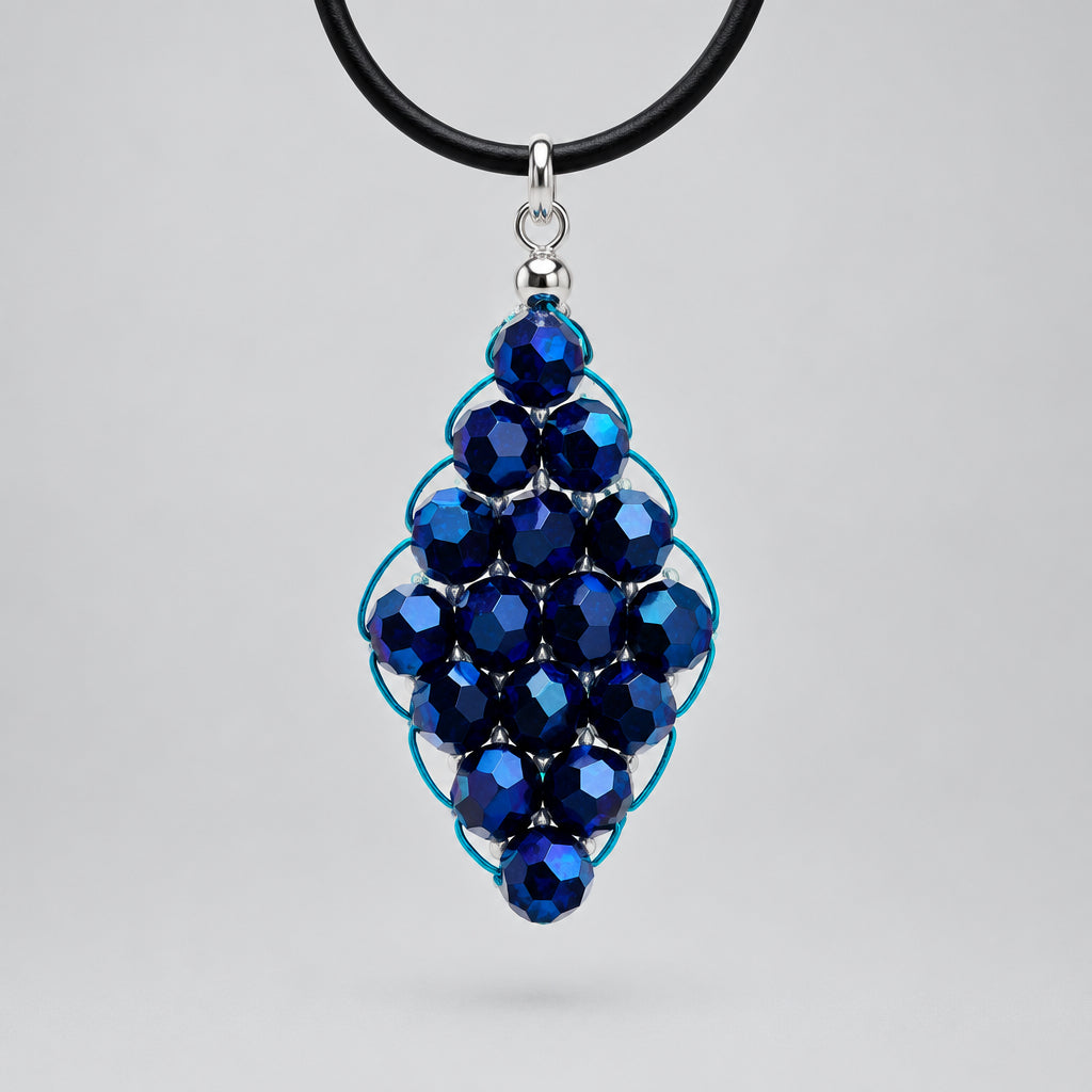 A handmade pendant necklace featuring dark blue faceted glass beads wrapped in turquoise wire, suspended from a black cord with a silver clasp, set against a textured white background.