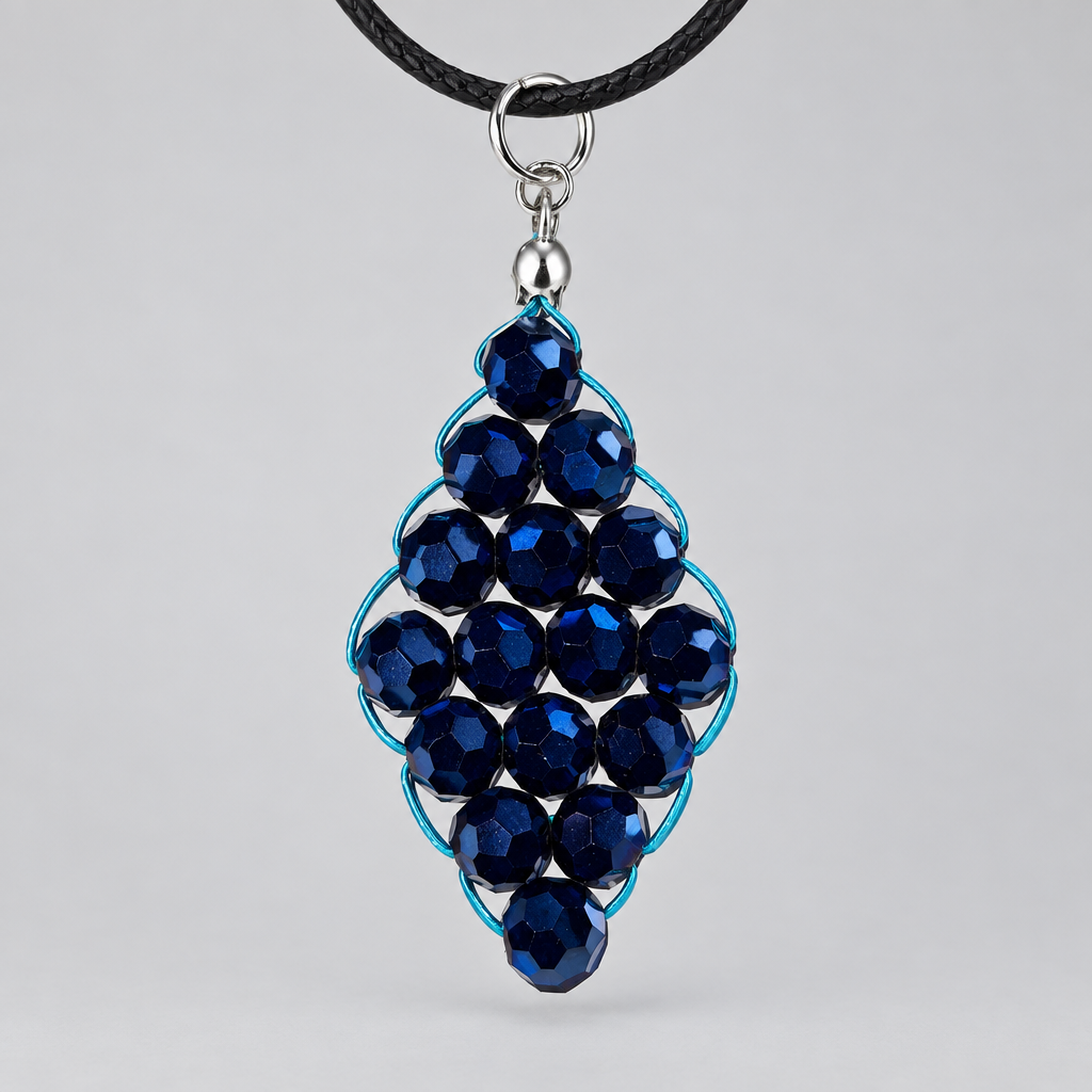 A close-up of a handmade pendant necklace featuring faceted dark blue beads wrapped in light blue wire, suspended from a black cord with a silver metal ring, set against a textured off-white background.