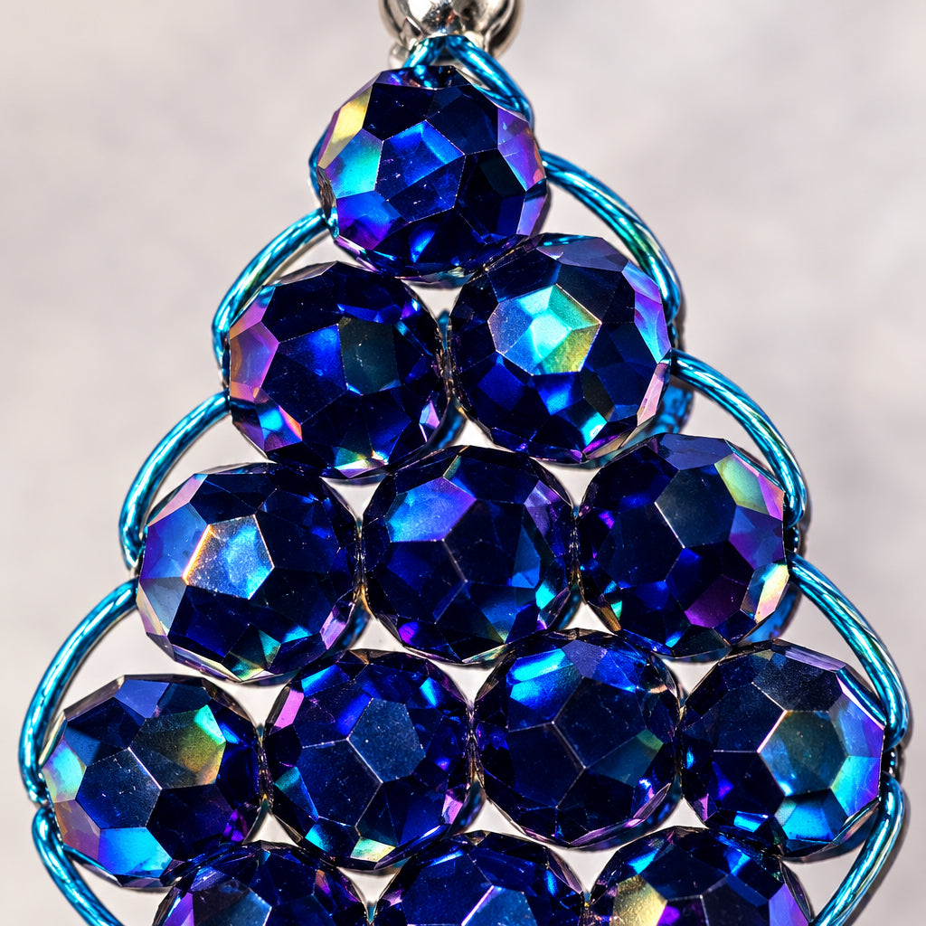 A close-up of a handmade keychain charm featuring faceted dark blue beads arranged in a teardrop pattern, wrapped in light blue wire and attached to a silver metal ring, set against a textured off-white background.