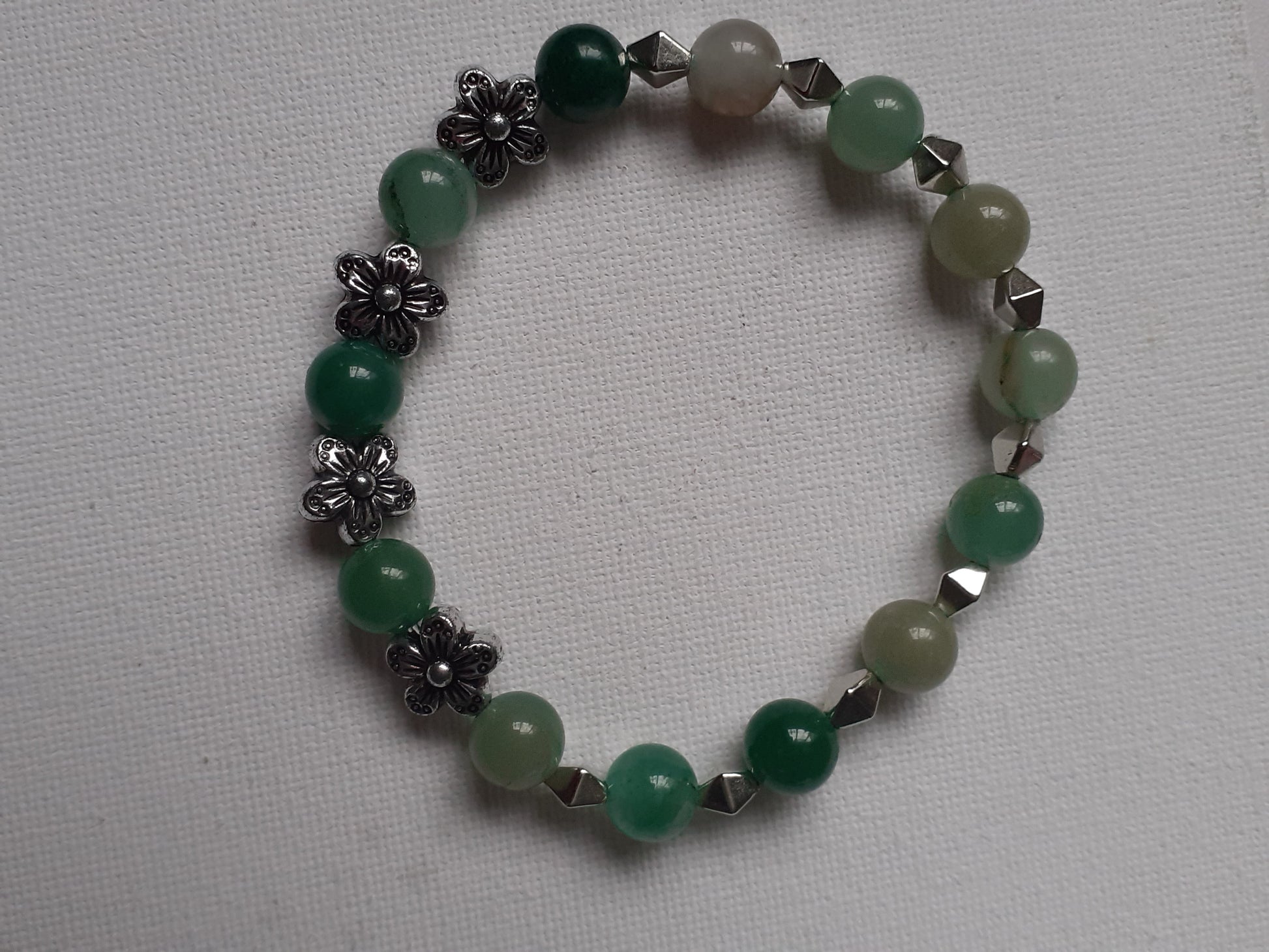Green beaded bracelet with silver floral and geometric accents on a light gray background