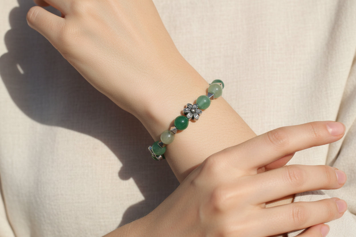 Hand wearing a green beaded bracelet on a neutral background