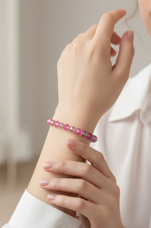 A close-up of a person's wrist wearing a beaded bracelet made of faceted pink and clear heart-shaped crystals, styled with a white collared shirt.