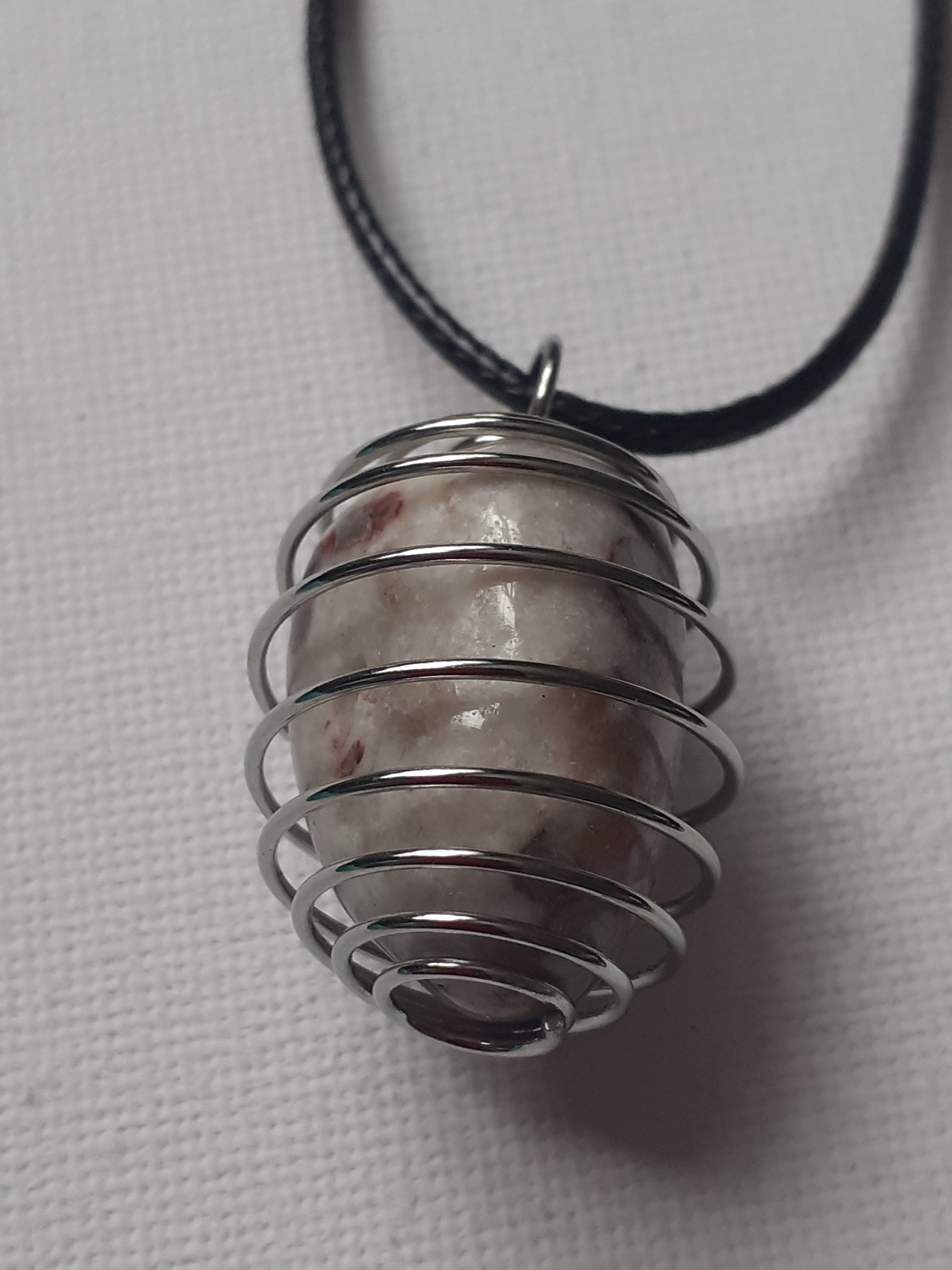 Metallic spiral pendant on a black cord against a light gray background