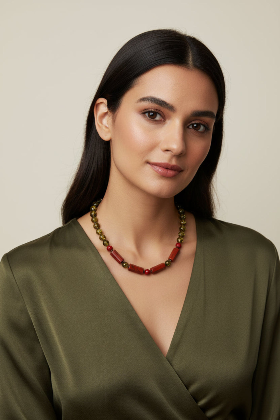 Woman wearing a green dress and red and gold necklace against a beige background