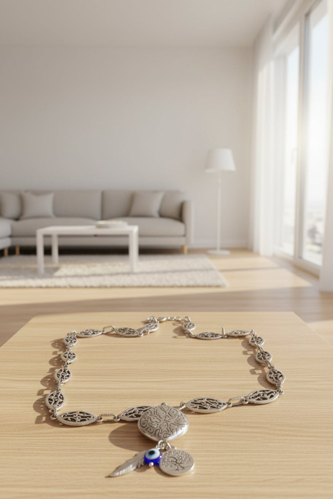 Silver necklace with charms on a wooden surface in a bright room with a sofa and lamp.