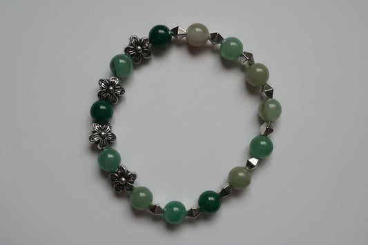 Green beaded bracelet with silver floral and geometric accents on a light gray background