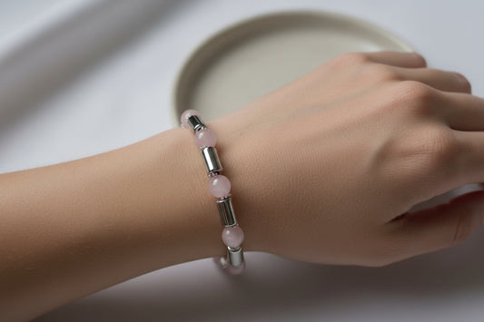Hand wearing a pink beaded bracelet with silver accents on a light background